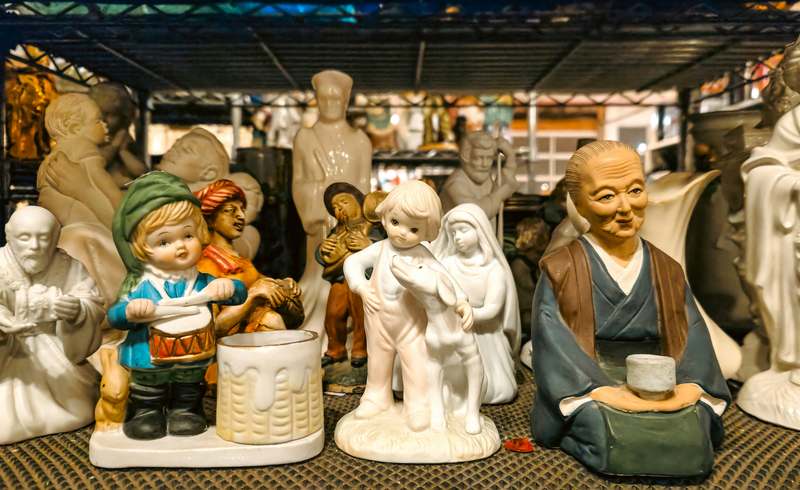 Close-up of hand-painted ceramic figurines on a linen-draped table beside design books and a potted succulent